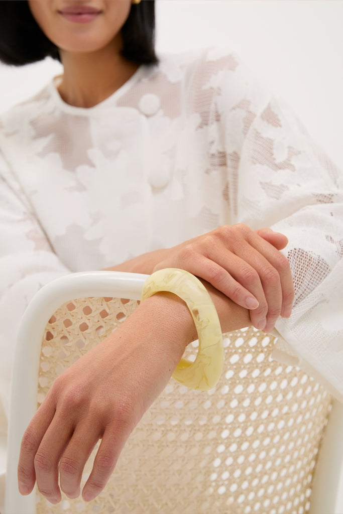 Close-up of a person wearing a sheer top, showcasing the Lemon Rock Small Bangle in marbled pale-yellow resin, exuding effortless, high-end style with a classic, fun twist.