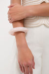 Person wearing classic off-white attire showcases the Swirl Rose Rock Small Bangle, an effortless, high-end accessory, adding a fun, stylish touch to their look.