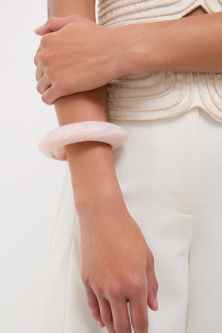 Person wearing classic off-white attire showcases the Swirl Rose Rock Small Bangle, an effortless, high-end accessory, adding a fun, stylish touch to their look.