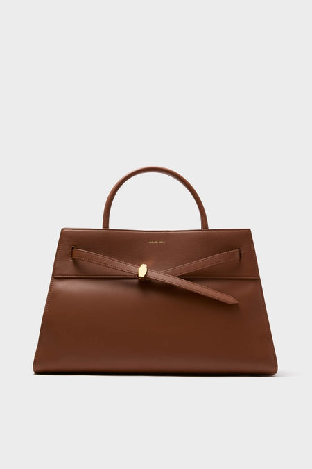Hazelwood Large Veronica Beard Dash Bag, a classic trapezoidal top-handle handbag in smooth leather, featuring an adjustable knotted strap with gold accent. Effortless and high-end design.