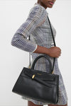 Person wearing a classic, effortless multi-colored tweed dress, carrying a high-end Black Veronica Beard Dash Bag with fun structured handles and versatile shoulder strap.