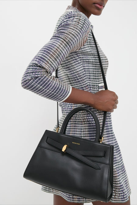 Person wearing a classic, effortless multi-colored tweed dress, carrying a high-end Black Veronica Beard Dash Bag with fun structured handles and versatile shoulder strap.