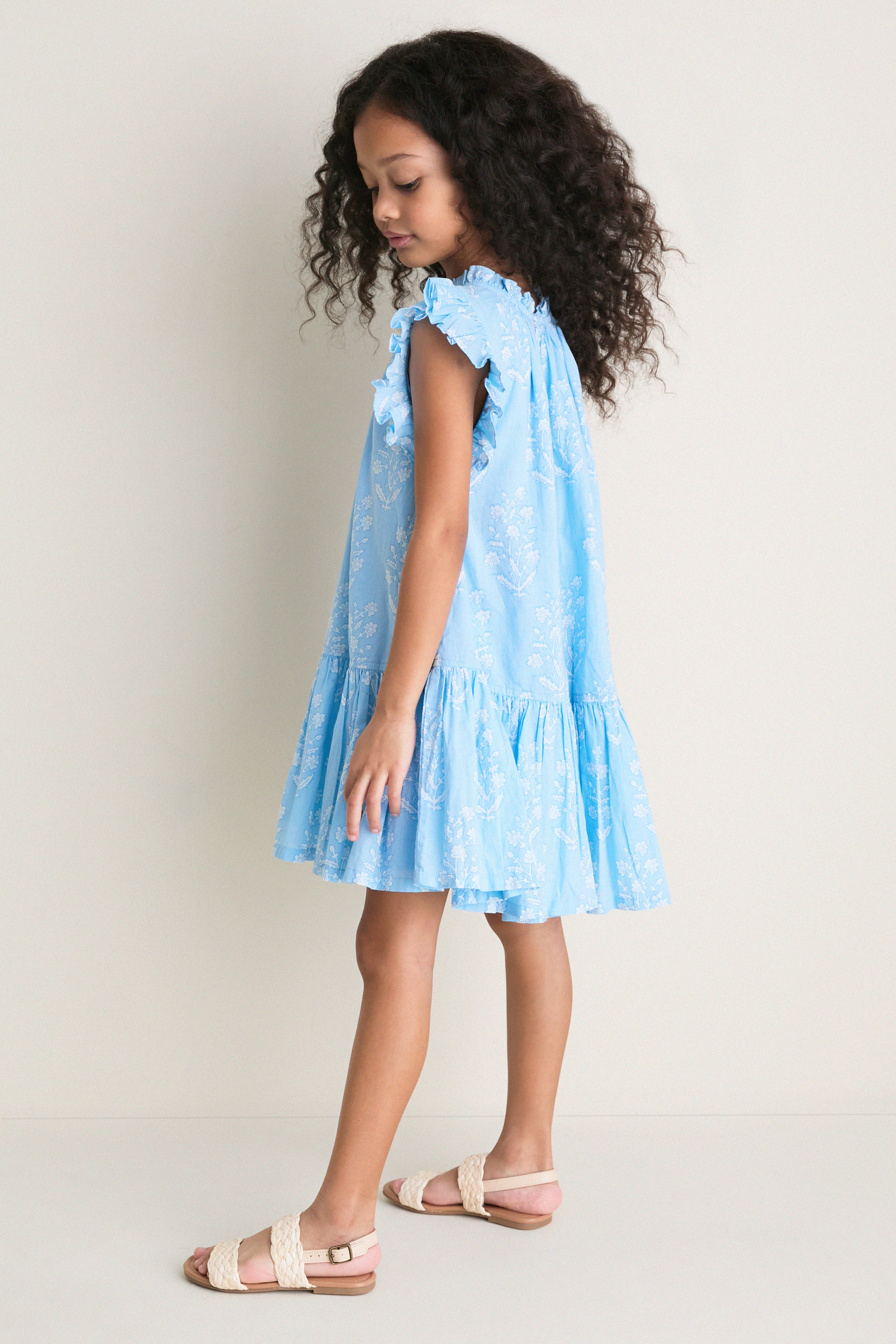 Young girl in profile wearing the classic Blue Dewdrop Block Print Harper Dress, showcasing effortless charm with ruffled sleeves and a fun, high-end flouncy silhouette.