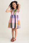 Young girl in a classic, playful Plaid Madras Alyssa Dress, featuring ruffles and patch pockets, embodying effortless style and fun, paired with brown leather sandals.