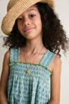 Young girl in classic Blue Prairie Block Print Eleven Jumper with smocked bodice, wide legs, and green pearl stitches, exuding effortless, high-end charm and fun.