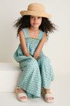 Young girl in a classic Blue Prairie Block Print Eleven Jumper with floral motifs, smocked bodice, and espadrille sandals, exuding effortless charm and high-end playfulness.