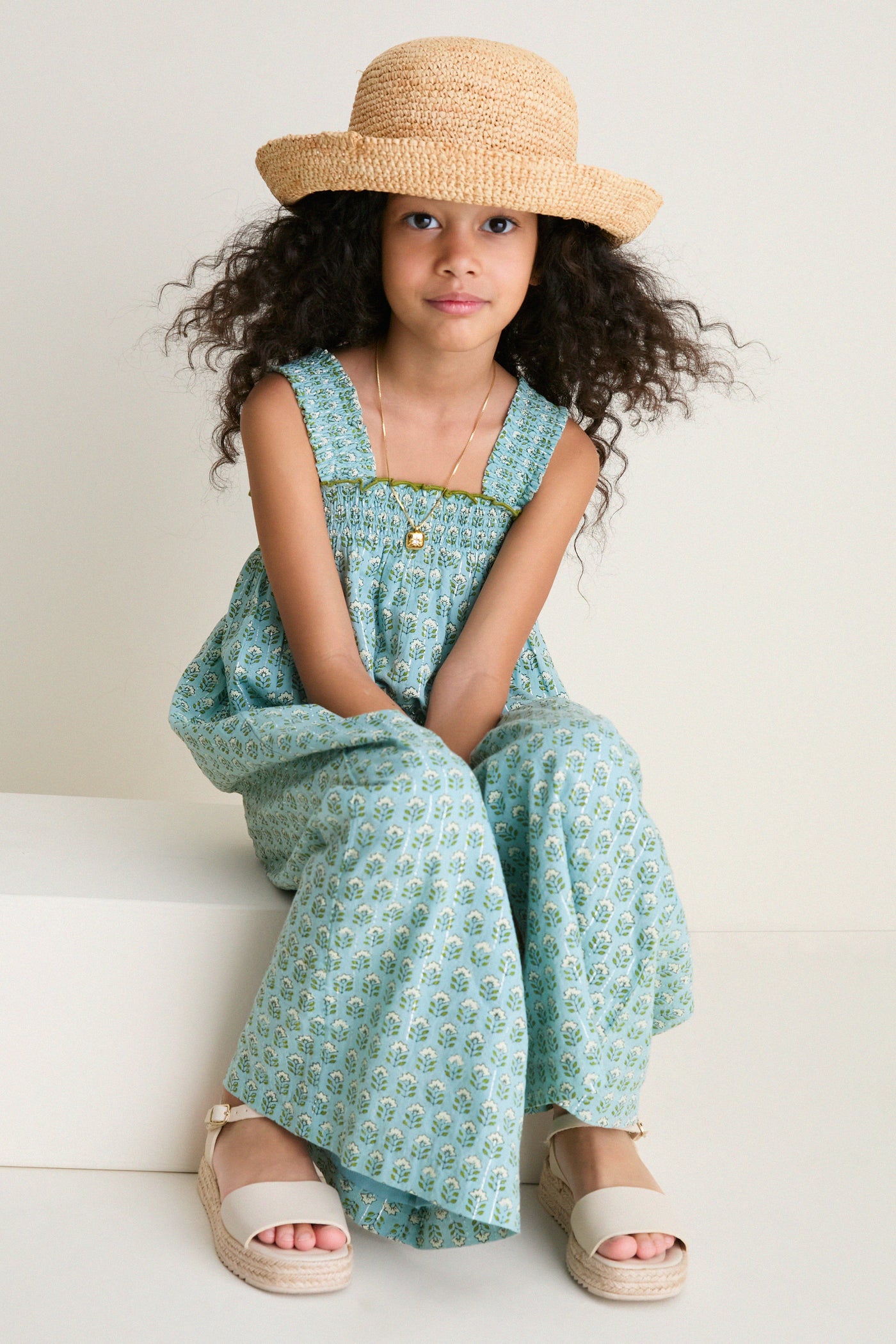 Young girl in a classic Blue Prairie Block Print Eleven Jumper with floral motifs, smocked bodice, and espadrille sandals, exuding effortless charm and high-end playfulness.