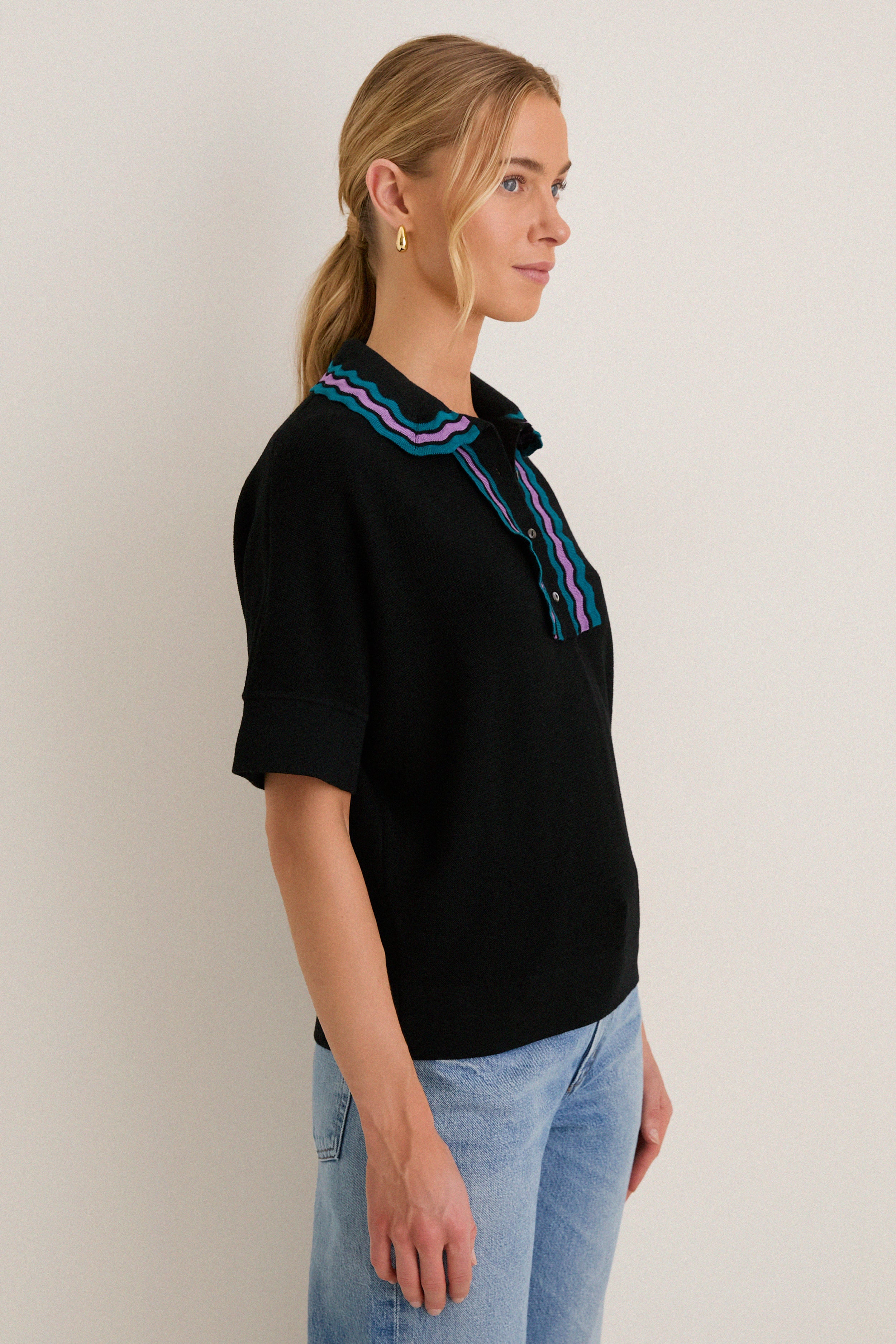 Woman in profile wearing the Deep Black Multi Polo Sweater, showcasing its classic, effortless design with a playful ric-rac collar, paired with light-wash jeans.