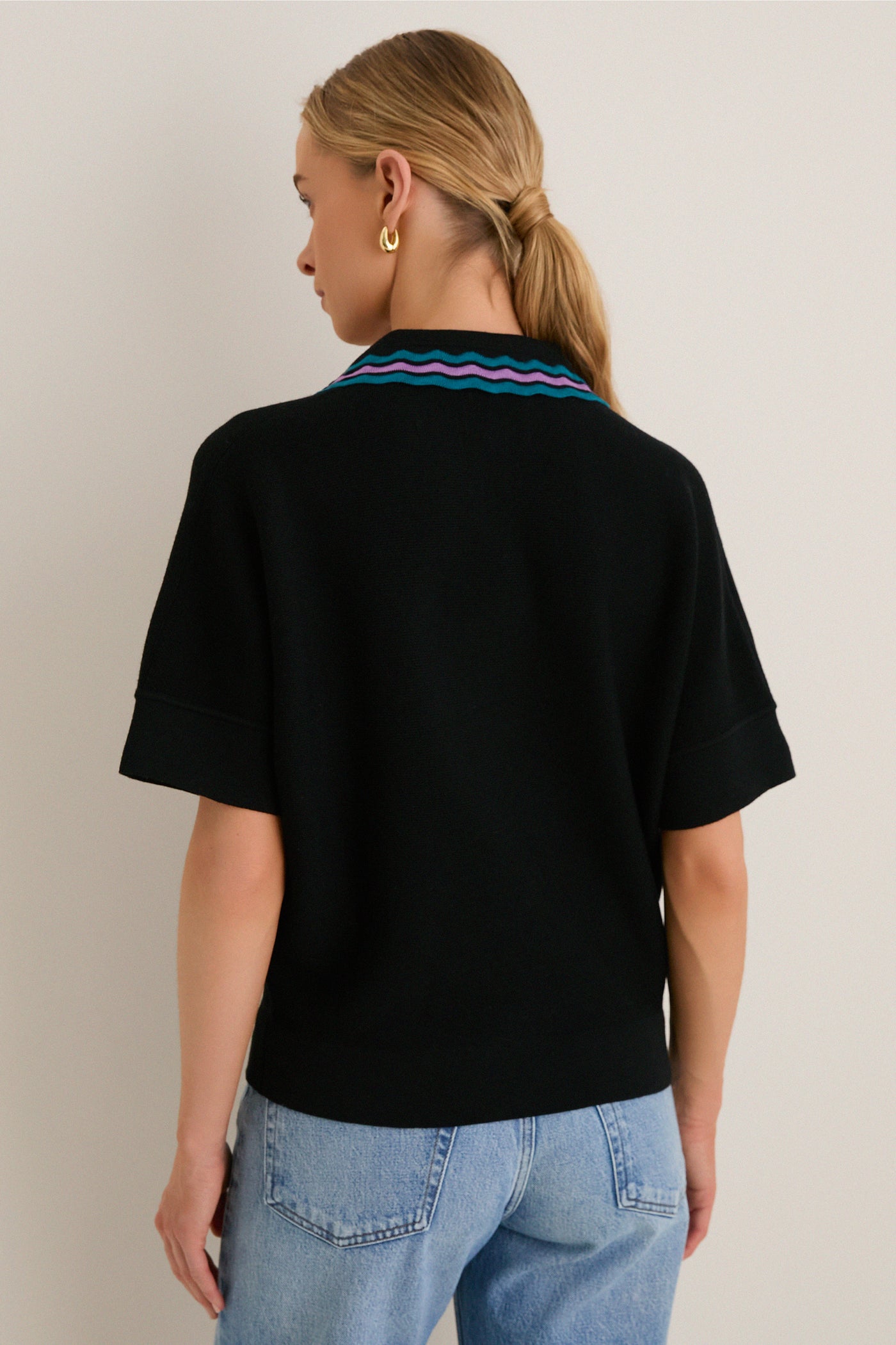 Back view of a young woman in a Deep Black Multi Polo Sweater with playful teal, lavender, and blue ric-rac collar, styled effortlessly with light-wash jeans.