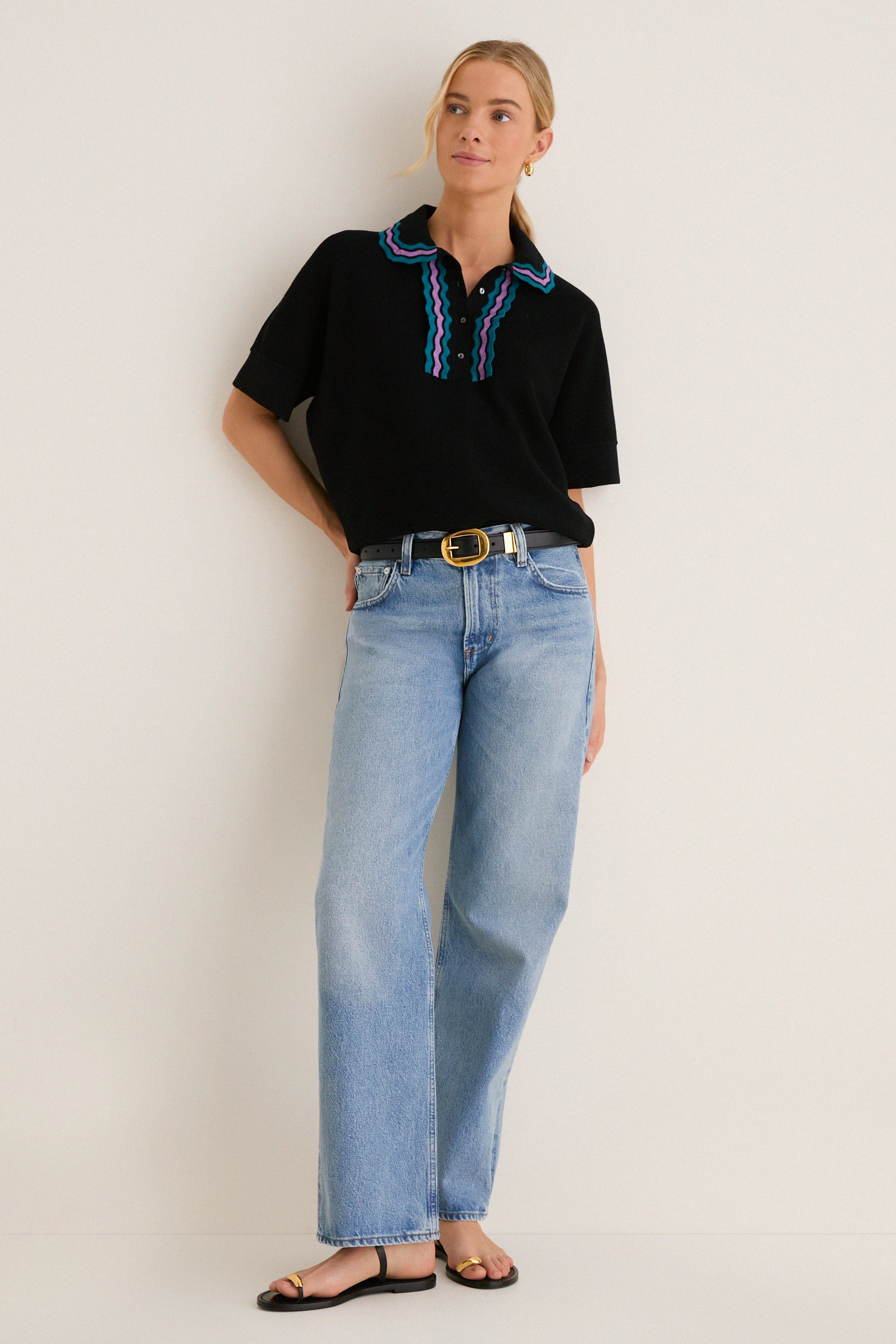 Young woman in a high-end, classic black polo sweater with playful purple and teal trim, paired with effortless light-wash jeans, embodying a fun, confident style.