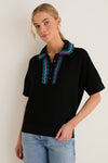 Woman in a classic, effortless Deep Black Multi Polo Sweater with playful teal and purple ric-rac details, paired with light-wash jeans, exuding a high-end, fun vibe.
