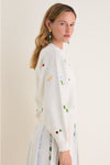 Young woman in a classic Milk Multi Dump Sweater with embroidered motifs, embodying an effortless, high-end style. Perfectly paired with a playful, fun knit skirt.