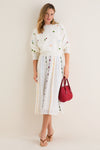 Woman models Milk Multi Dump Sweater with floral embroidery and smocked cuffs, styled effortlessly with a matching skirt, exuding a classic and fun high-end spring look.