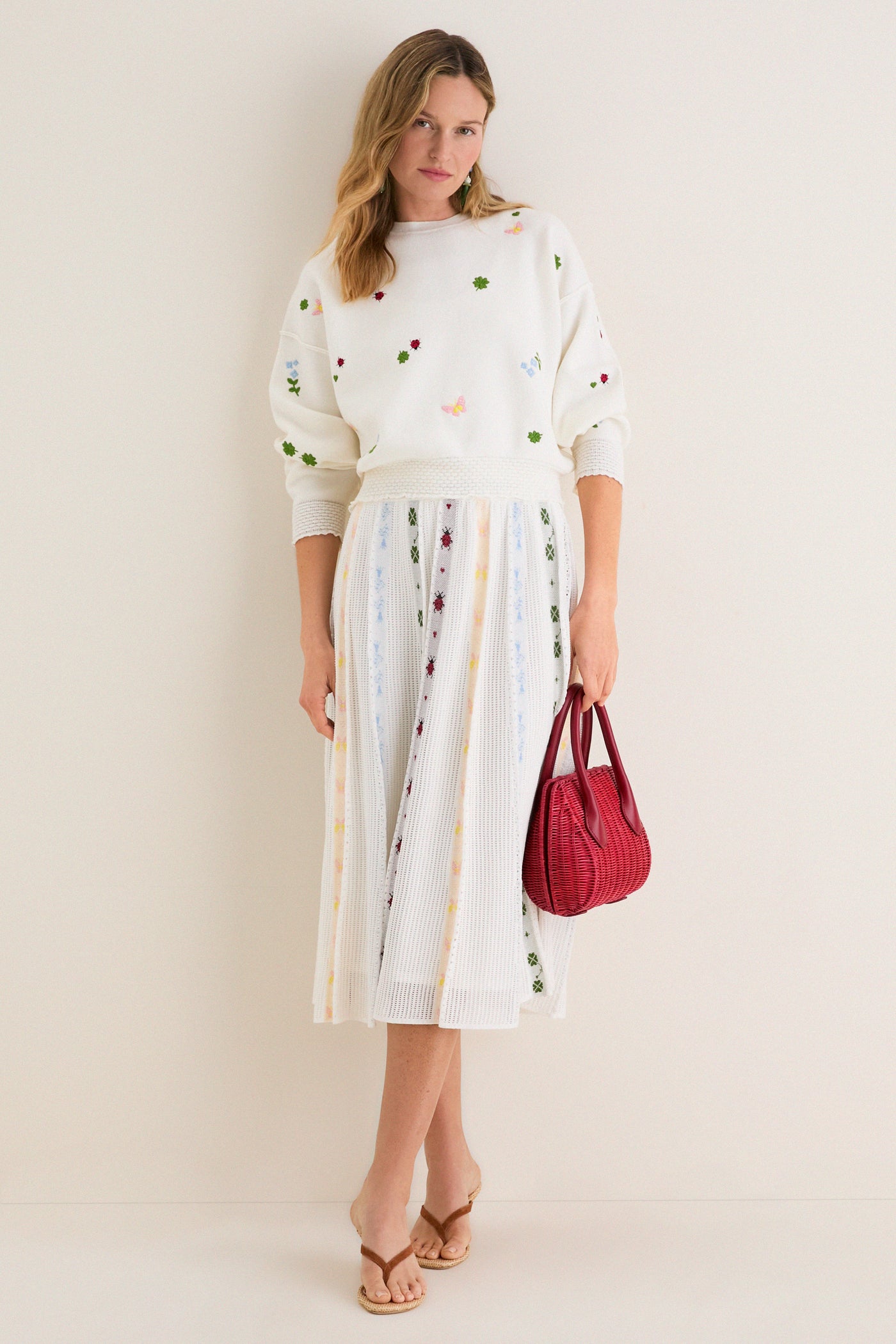 Woman models Milk Multi Dump Sweater with floral embroidery and smocked cuffs, styled effortlessly with a matching skirt, exuding a classic and fun high-end spring look.