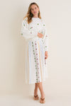 Woman in a classic, embroidered Milk Multi Dump Sweater and matching skirt, exuding an effortless, fun, high-end style with colorful earrings and brown sandals.