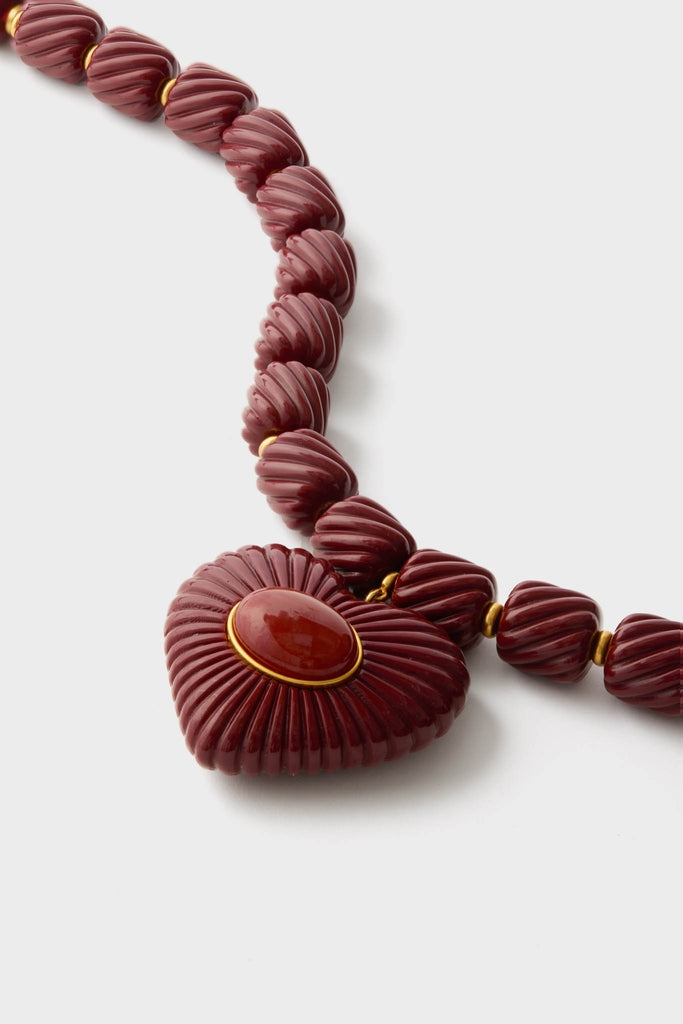 Burgundy Lira Necklace: A classic, high-end piece with fluted burgundy beads and a heart-shaped pendant, offering an effortless, fun elegance with gold accents.