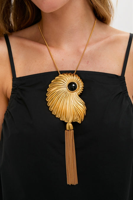 Gold Aveline Necklace with a nautilus-inspired pendant, featuring a central black stone and a gold chain tassel, exudes classic, effortless elegance for a fun, high-end look.