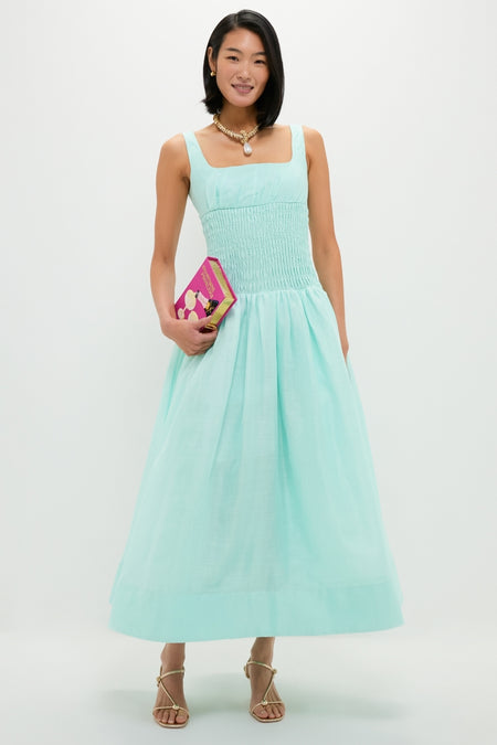 A woman models an effortless, high-end look with a classic gold pearl drop necklace, showcasing chic elegance alongside a stylish aqua dress and gold accessories.