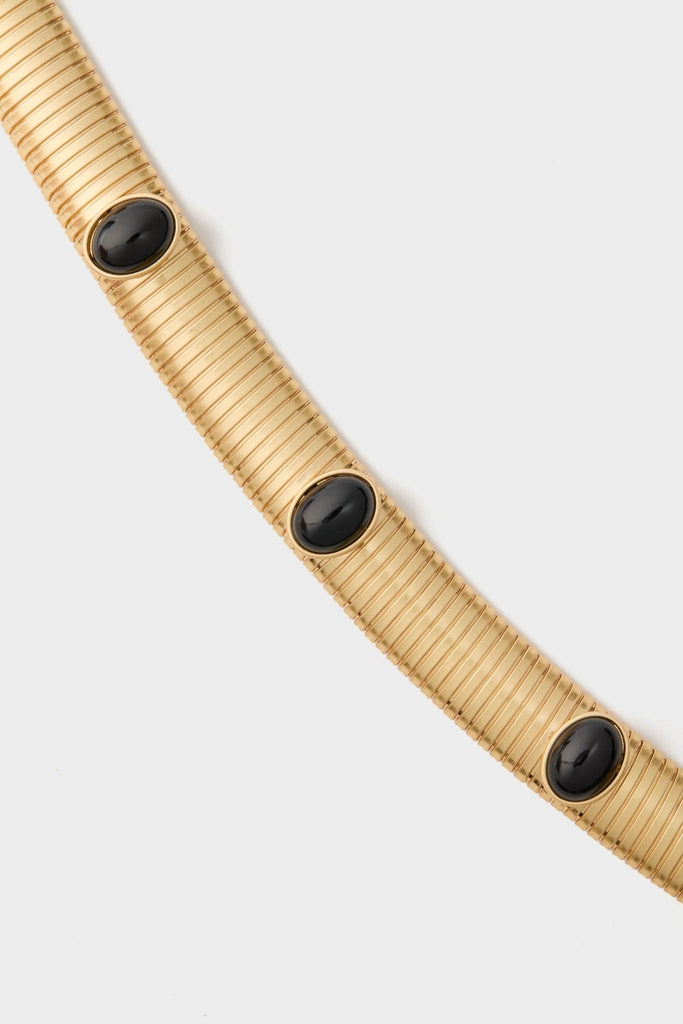 Gold Celeste Necklace: A classic, high-end choker with ribbed gold-tone metal, featuring effortless elegance through smooth, oval black cabochon stones for a fun, confident style.