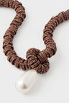 Brown Pearl Drop Necklace: A classic, high-end piece featuring bronze-colored metal rings with sparkly stones, tied in a knot, ending in an effortless, fun teardrop-shaped pearl pendant.