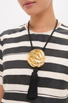 Person wearing the Gold and Black Hebe Necklace, featuring a classic gold-tone medallion with a black tassel on a thick cord, exuding effortless, fun, high-end style.