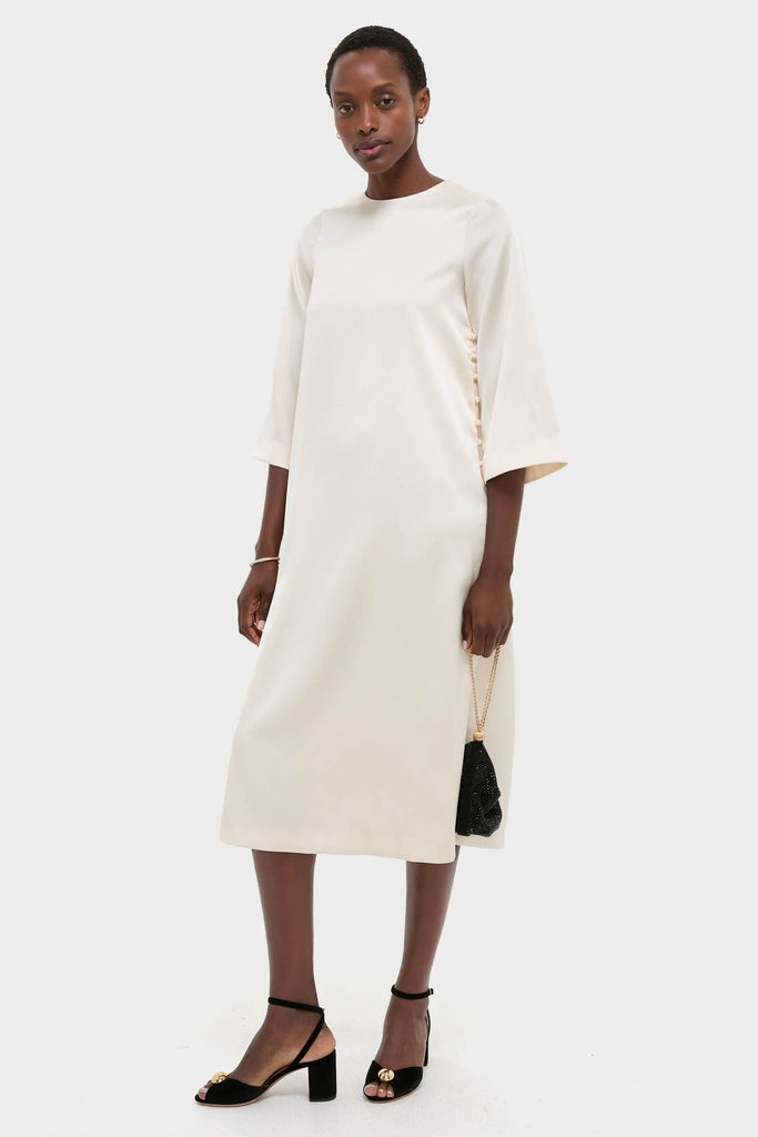 Woman in a classic cream dress accessorized with a Gold and Pave Tubular Bracelet, exuding an effortless, high-end look with fun black heels and a chic bag.