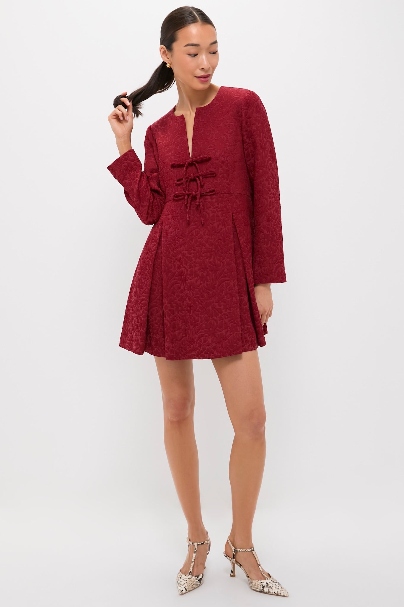 Woman in Cranberry Jacquard Blair Bow Dress, featuring classic A-line silhouette, keyhole neckline, and embossed floral pattern, paired with T-strap heels for an effortless, high-end look.