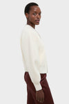 Person wearing the Ivory Sequin Trim Naomi Cardigan, a classic, oversized knit sweater paired with burgundy pants, exuding an effortless, high-end style.