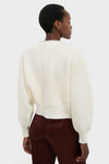 Person wearing the Ivory Sequin Trim Naomi Cardigan, a classic knit sweater with dropped shoulders and balloon sleeves, paired with high-end burgundy pants, embodying an effortless and fun style.