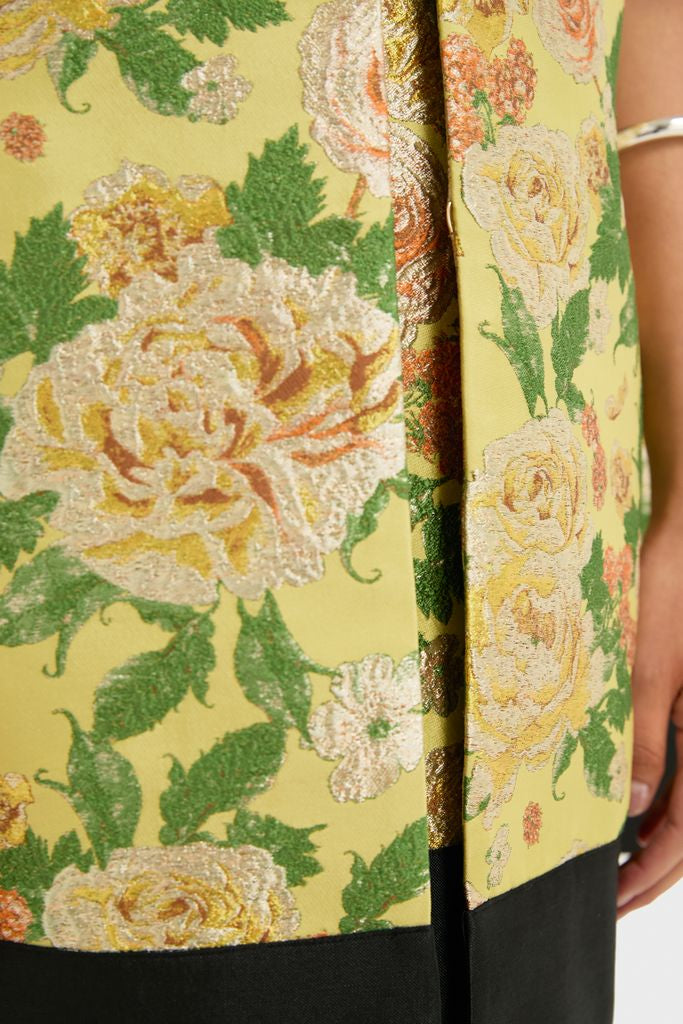 Chrysanthemum Jacquard Noel Cape in yellow brocade with metallic floral pattern, black hem, and silver-bangle-adorned arm, offering a classic, effortless, and high-end style.