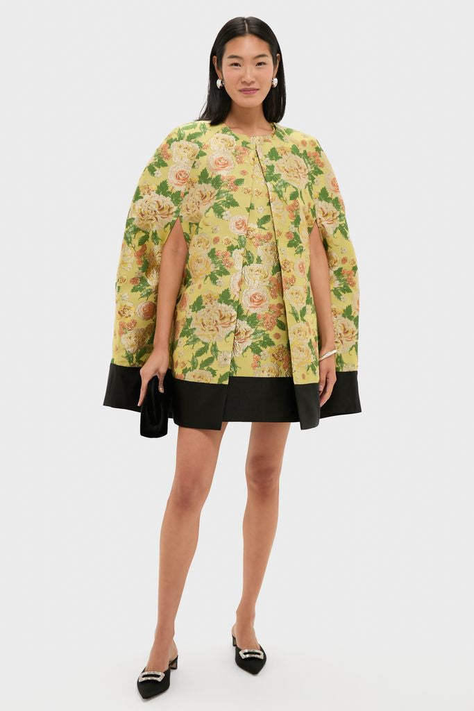 Woman models the classic Chrysanthemum Jacquard Noel Cape, featuring an effortless floral-brocade design with shoulder slits, styled with pearl earrings and a black clutch.
