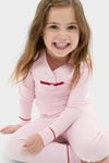 Young girl in Pink Arien Kid's Pajama Set with red trim and ribbon, exuding classic, effortless style and comfort, embodying Tuckernuck's fun, high-end shopping experience.