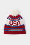 USA Telluride Hat: A classic knitted beanie with red, white, and blue stripes, USA letters, and a fluffy pom-pom, offering effortless, fun, high-end winter style.