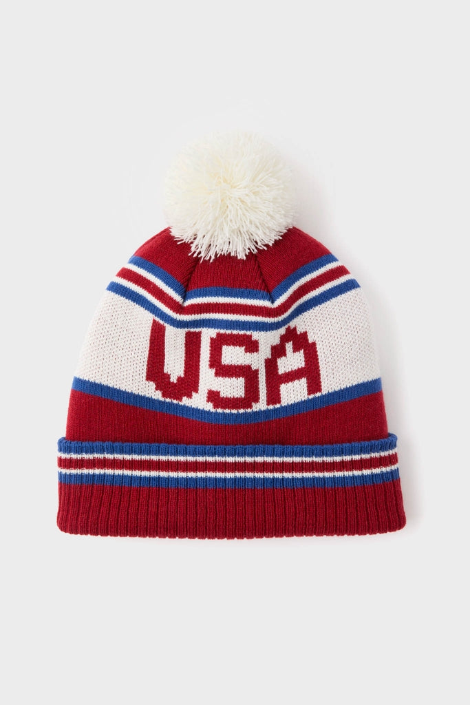 USA Telluride Hat: A classic knitted beanie with red, white, and blue stripes, USA letters, and a fluffy pom-pom, offering effortless, fun, high-end winter style.