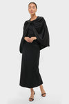 Woman wearing a classic Black Satin Mountbatten Cape, elegantly draped over a sleek black dress, embodies an effortless, high-end style with fun, matching black accessories.