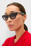 Woman wearing Shiny Black Cat-Eye Mods Sunglasses with Gucci logo, styled with gold hoop earrings and a red knit top, embodying a classic, effortless, and high-end fashion look.