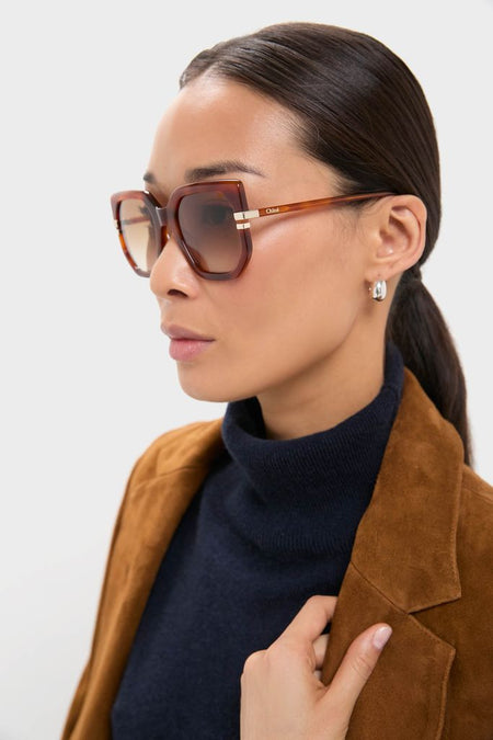 Woman models Shiny Blonde Havana West Sunglasses by Chloé, featuring oversized square frames in tortoiseshell acetate with gradient lenses, exuding a classic, effortless, and high-end style.