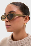 Person wearing Shiny Solid Licorice Brown Corner Angle M Sunglasses, exuding a classic and effortless vibe with high-end style, complemented by a chunky knit sweater and gold hoop earring.