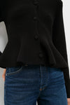 Black Knit Richmond Sweater with fabric-covered buttons and a peplum flare, paired with blue jeans, showcasing an effortless, classic, and high-end look.