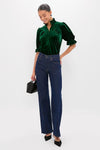 Woman models the Hunter Green Velvet Selena Top, showcasing classic elegance with a ruffle collar and puff sleeves, paired effortlessly with jeans and heels for a high-end, fun look.