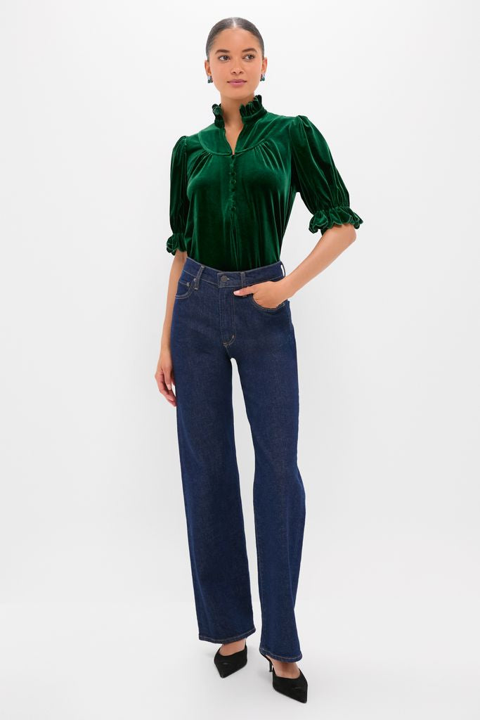 Woman in Hunter Green Velvet Selena Top with ruffled collar and puff sleeves, paired with dark jeans and heels, embodying classic, effortless, and high-end style.