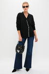 Woman models the Black Cross Button Calloway Cardigan with asymmetrical buttons and side cinch, paired with high-waisted jeans for an effortless, classic, high-end look.