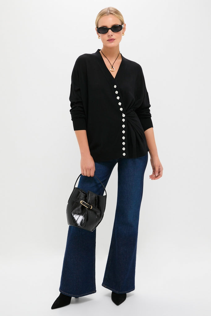 Woman models the Black Cross Button Calloway Cardigan with asymmetrical buttons and side cinch, paired with high-waisted jeans for an effortless, classic, high-end look.