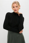 Woman wearing Black Pointelle Knit Allen Turtleneck with scalloped hem, styled with a high-waisted leather skirt. Effortless, classic, and high-end look with gold-trimmed earrings.