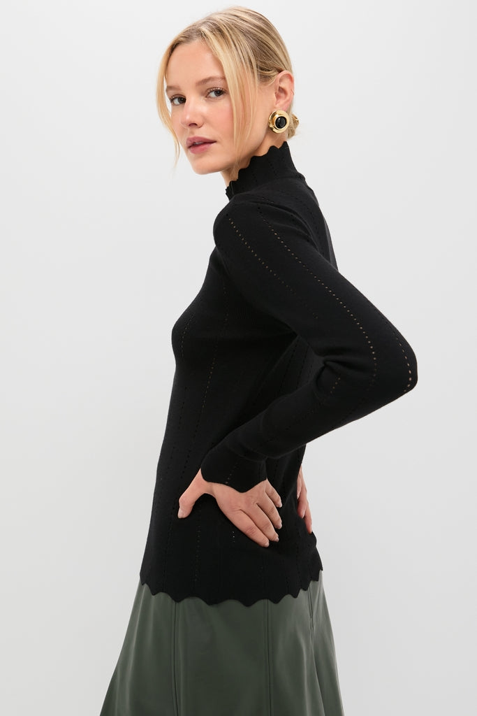Young woman models the Black Pointelle Knit Allen Turtleneck with scalloped trim, exuding classic, effortless style. Perfectly paired with an olive skirt for a high-end, fun look.