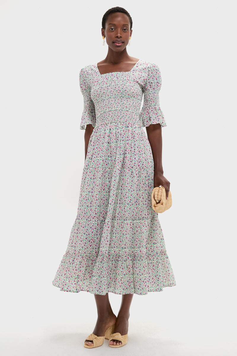 Primrose Print Bea Dress: Woman in a classic, effortless midi sundress with a floral pattern, puff sleeves, and tiered skirt, accessorized with a straw clutch and woven mules.