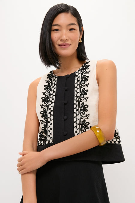 Young woman wearing the classic Soutache Cotton June Top with black embroidery and fabric-covered buttons, paired with a matching skirt. Effortlessly adorned with a chunky bangle and gold hoop earring.