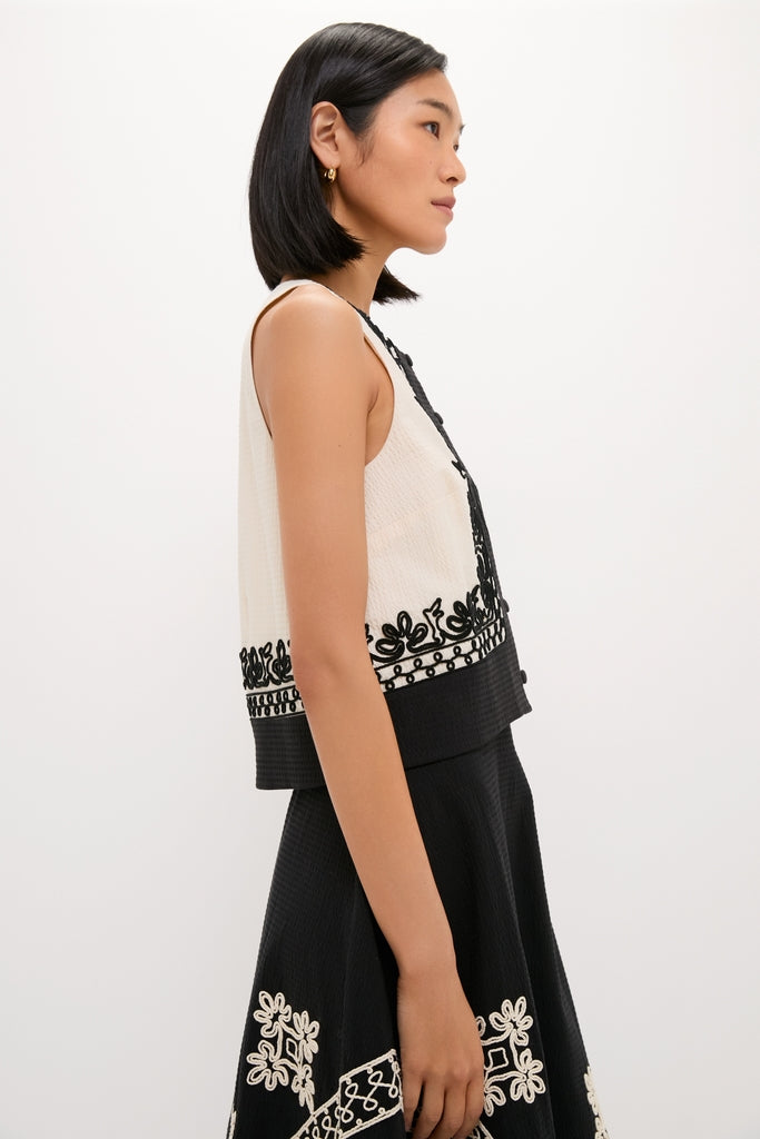 Young woman models classic Soutache Cotton June Top, featuring an off-white textured design with black embroidered trim, paired with an effortlessly chic black skirt.