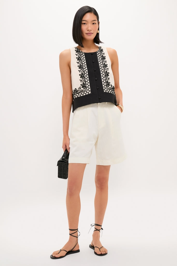 Young woman wearing the classic Soutache Cotton June Top with floral embroidery, paired with high-waisted shorts and lace-up sandals, holding a woven handbag for an effortless, high-end look.