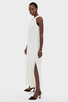 Model in classic Ivory Soleil Gown, featuring a sleeveless design, high neckline, and thigh-high slit. Paired with brown velvet slingback heels and gold accessories for an effortless, high-end look.